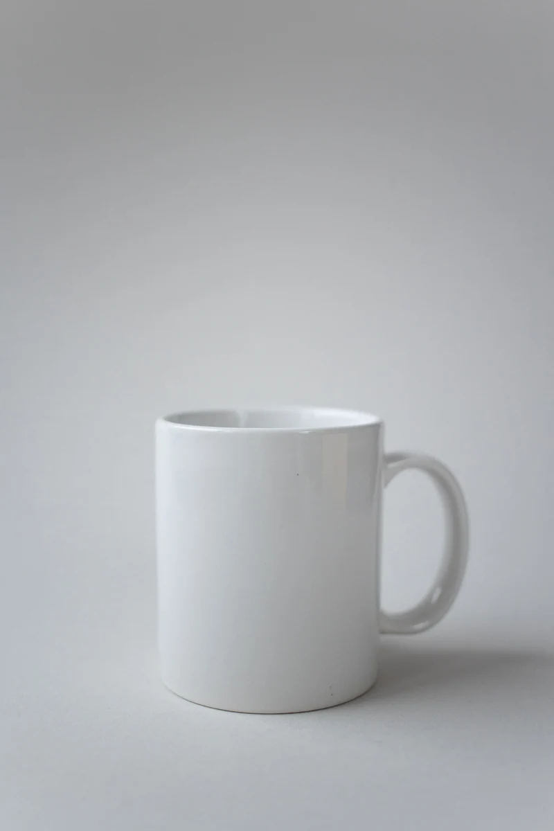 Original photograph of an unbranded white ceramic mug with a right-side handle on a pale surface